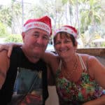 Couple smiling and wearing santa hats — Caravan Park in Kinka Beach, QLD
